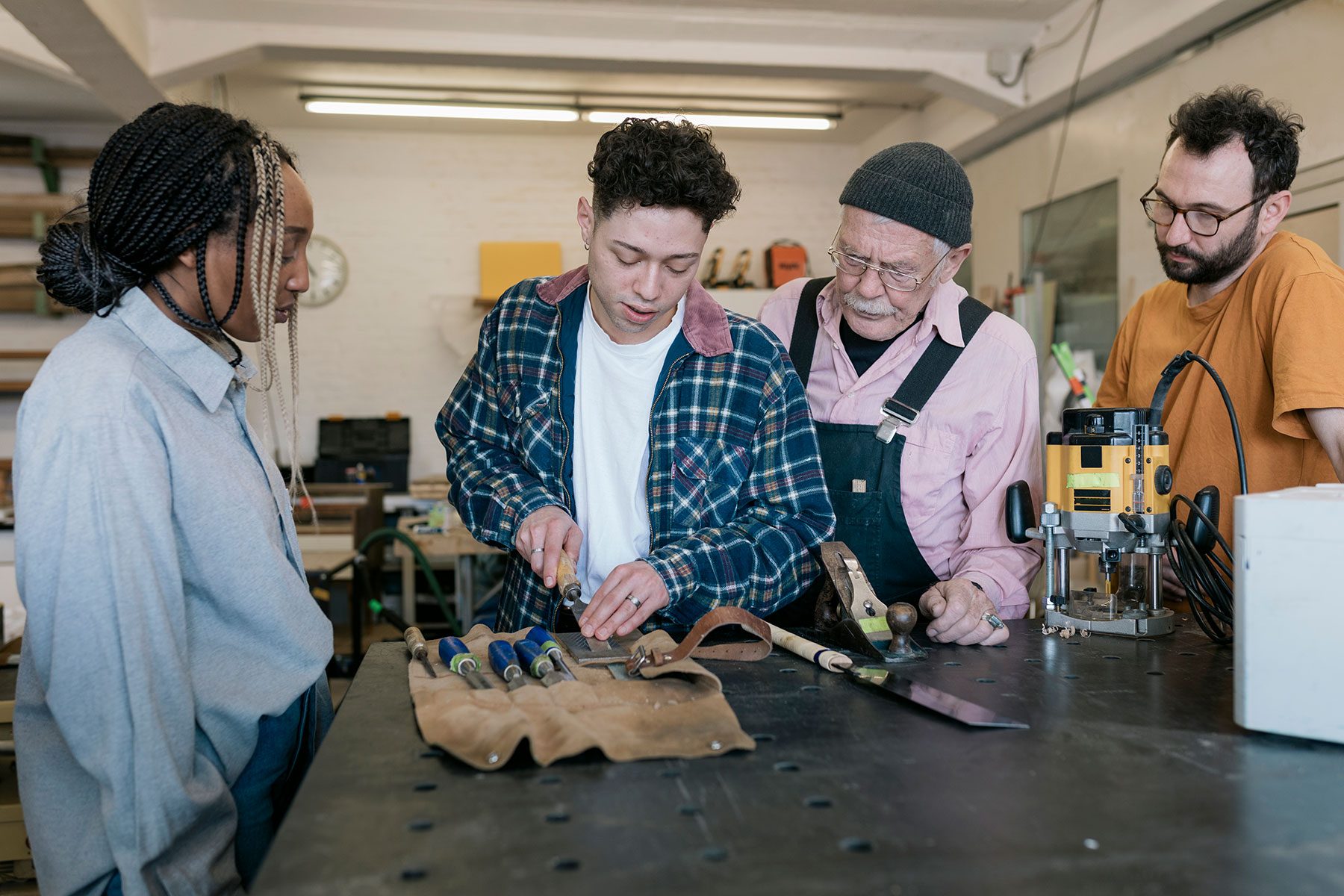 Interns Watching While Student Sharpens Chisel Set In Wood Workshop