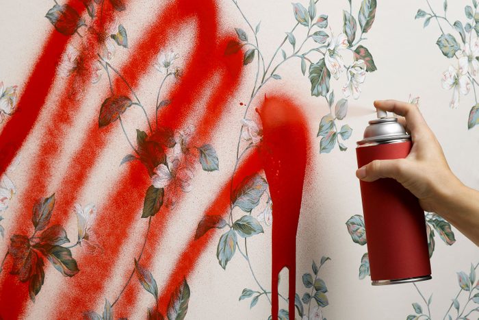 Female Hand Spray Painting floral and white Wallpaper with red spray paint can