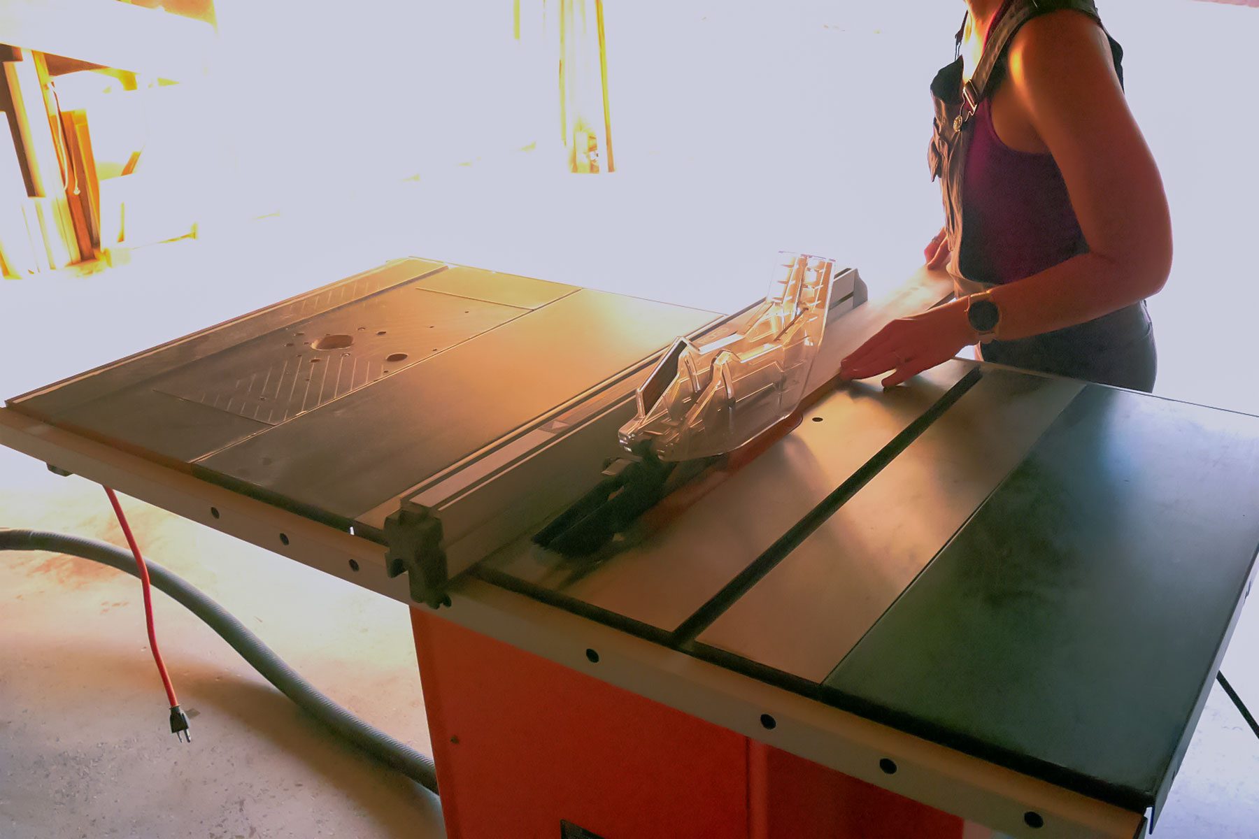 A woman working on a table saw in a garage.