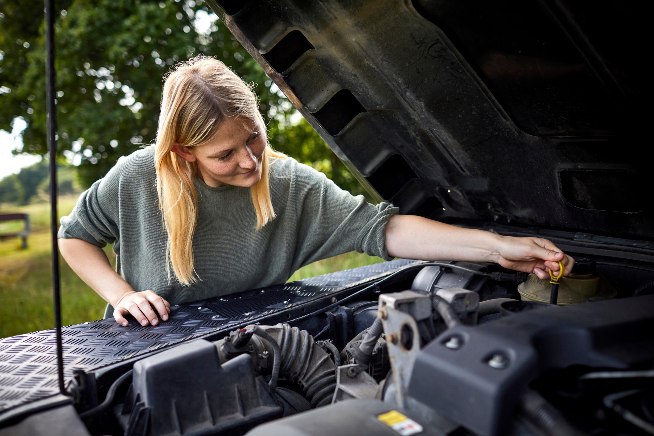 Young woman checking car with open hood