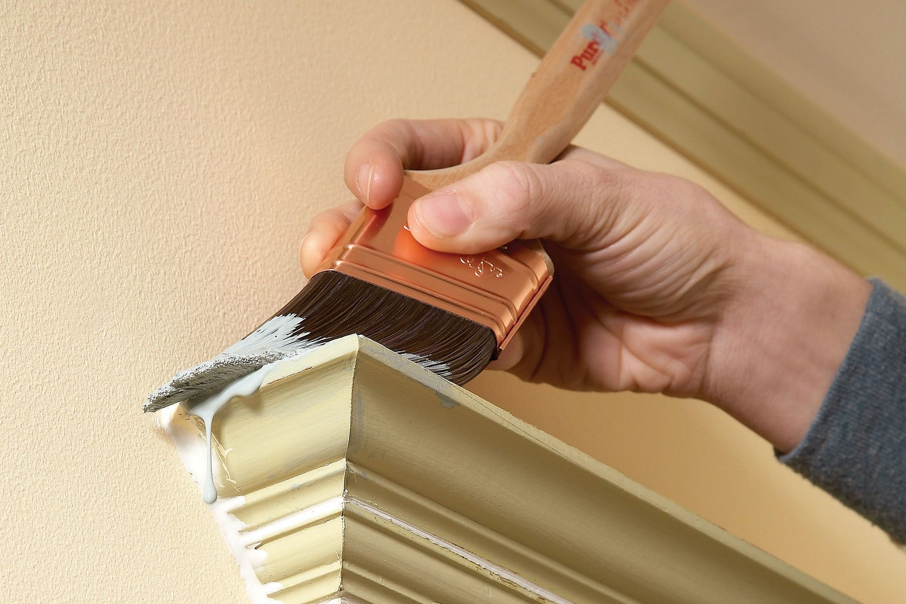 A person paints a the edges of a wall with a brush