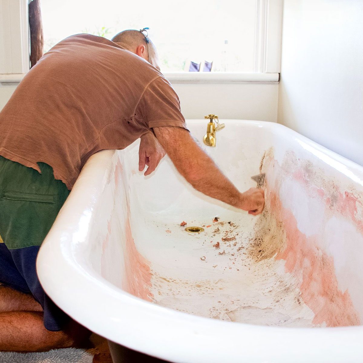 A Man Strips Away The Old Paint Of A Cast Iron Bathtub