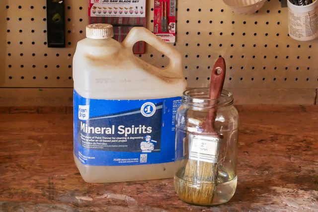 A brush inside a jar and a jar with mineral spirits placed on a wooden table
