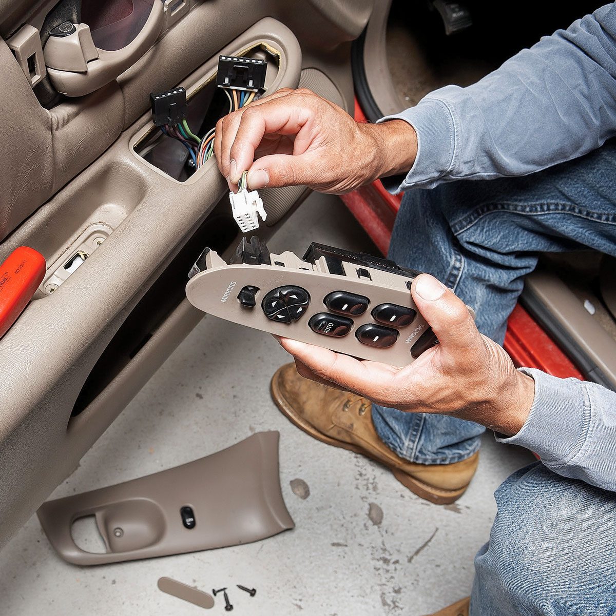 a person disconnecting electrical wires from a car's power window switch board