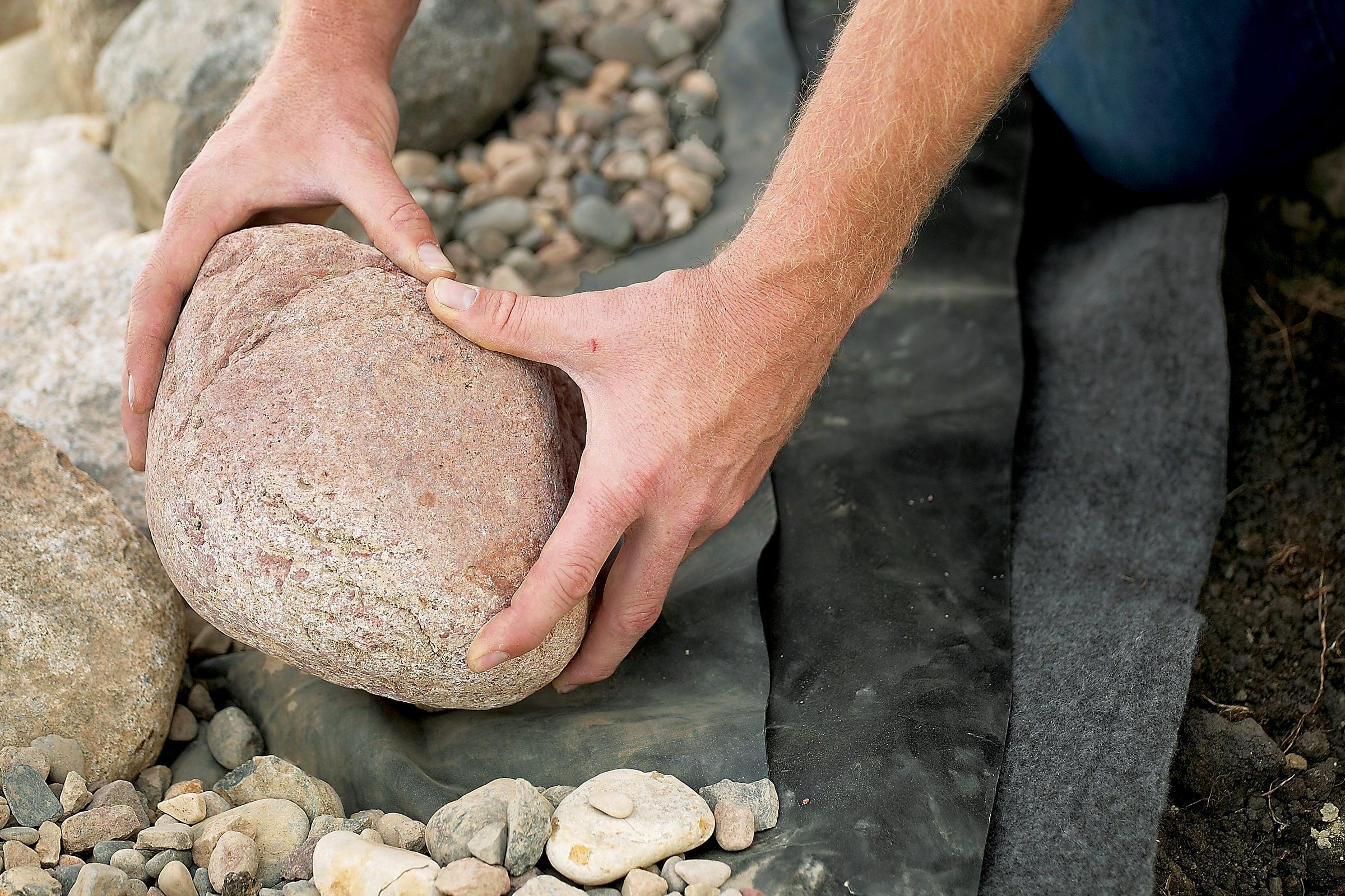 man with rock placing it around a pond and showing the padding that is beneath