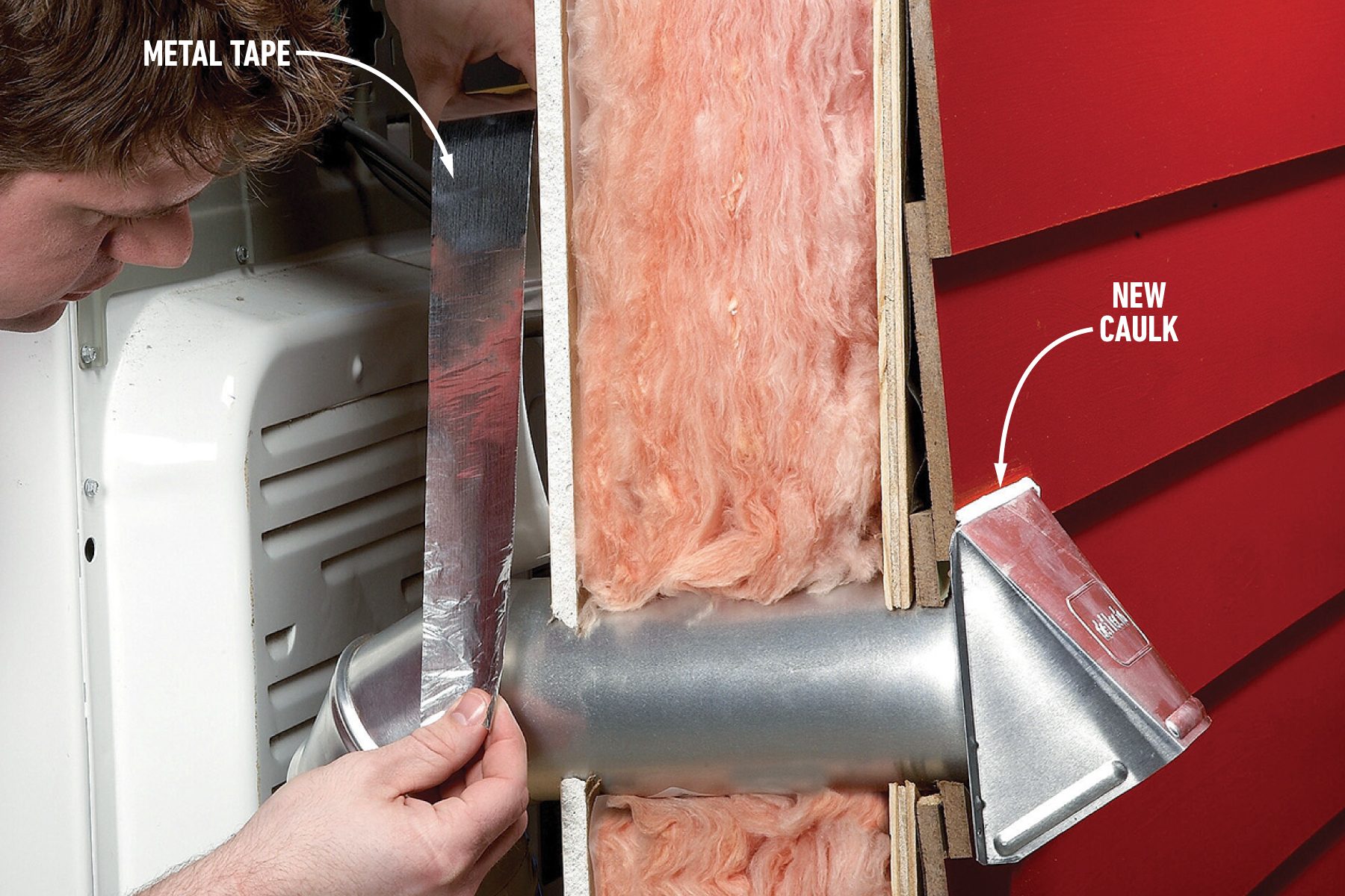 A person applies metal tape to a duct pipe protruding through an insulated wall with pink fiberglass insulation. A label points to an area of shiny, newly applied caulk on the right side of the pipe. The background wall is red.