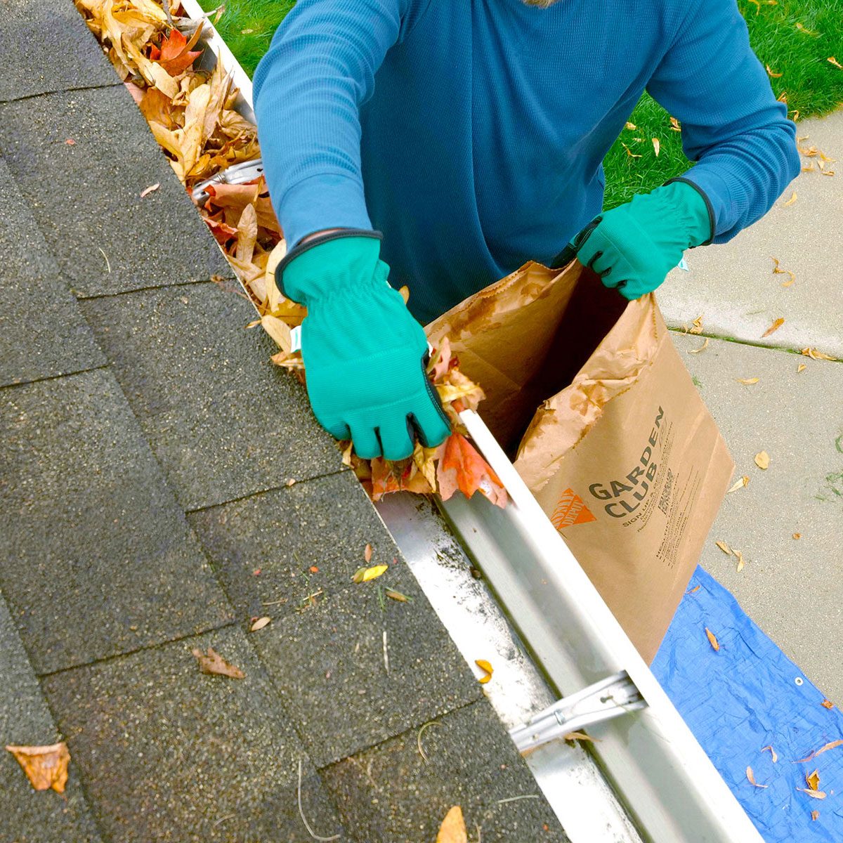 a person cleaning a clogged rain gutter full of dried leaves