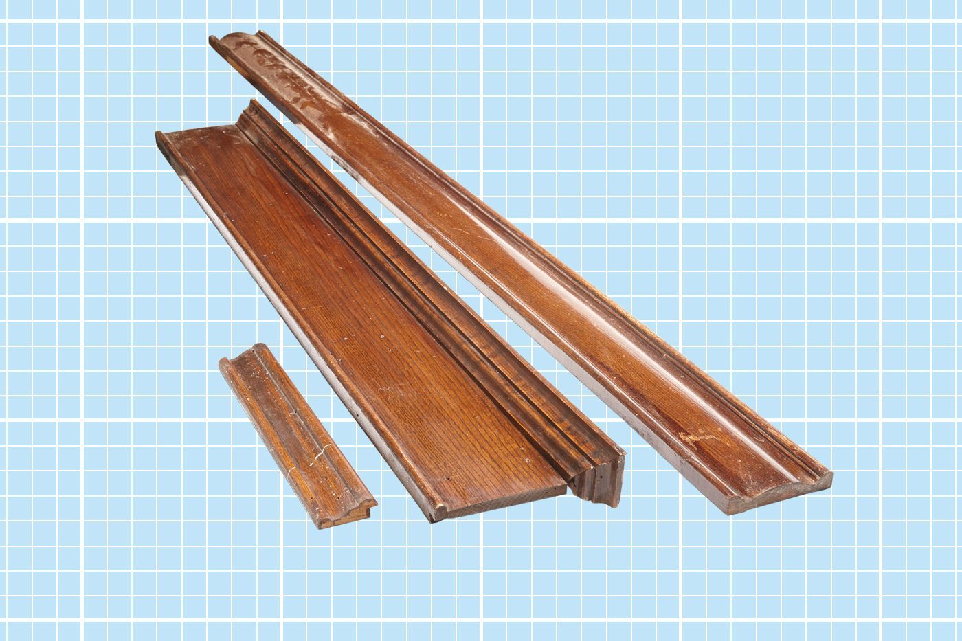 Several pieces of brown wooden molding or trim rest on a light blue grid background. The molding pieces vary in length and design, with one piece significantly shorter than the others. The wood has a polished finish.