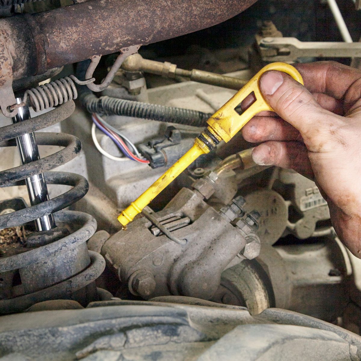 A hand holding a yellow dipstick is checking the oil level in a car’s engine.