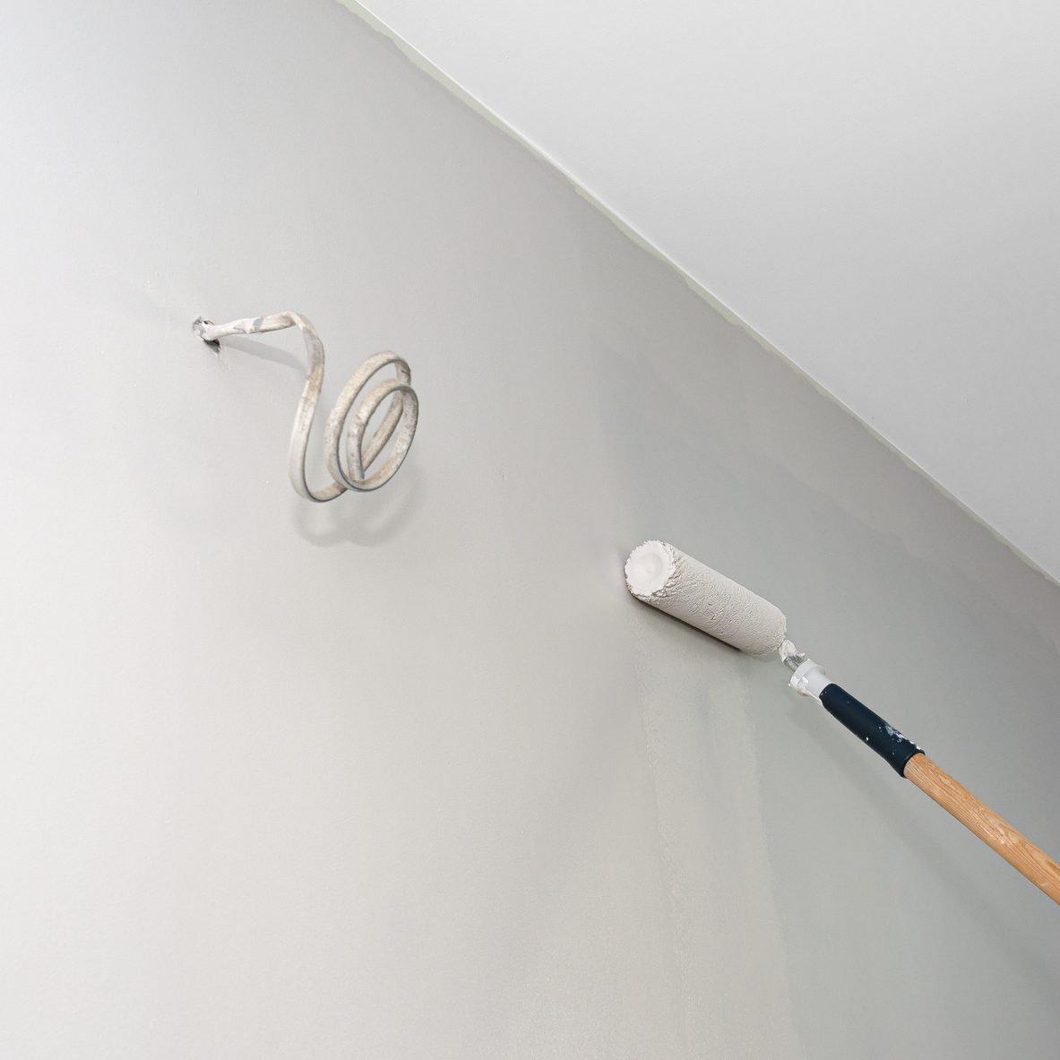 Painter paints a room in beige color using a paint roller on an extended stick at home.