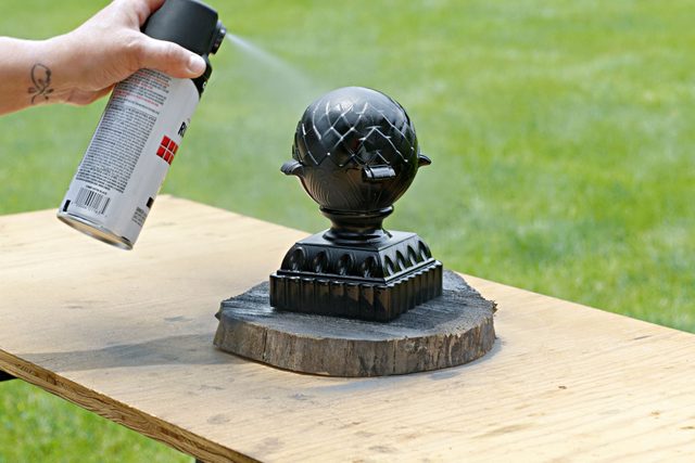 A hand can be seen painting the finial with spray paint from a can.