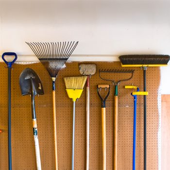 Household and garden tools stored in garage on pegboard wall in an organized and tidy fashion.