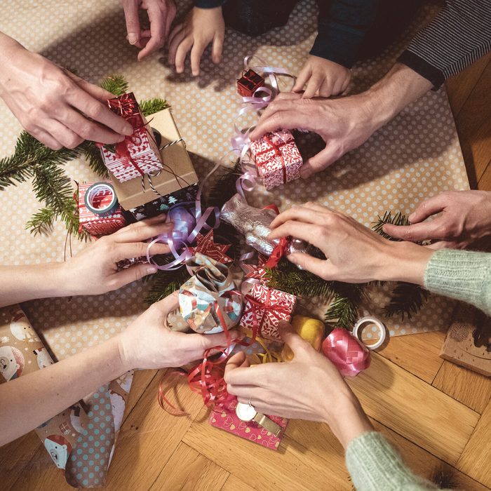 Many hands reach for Christmas gifts on the wooden floor for Secret Santa