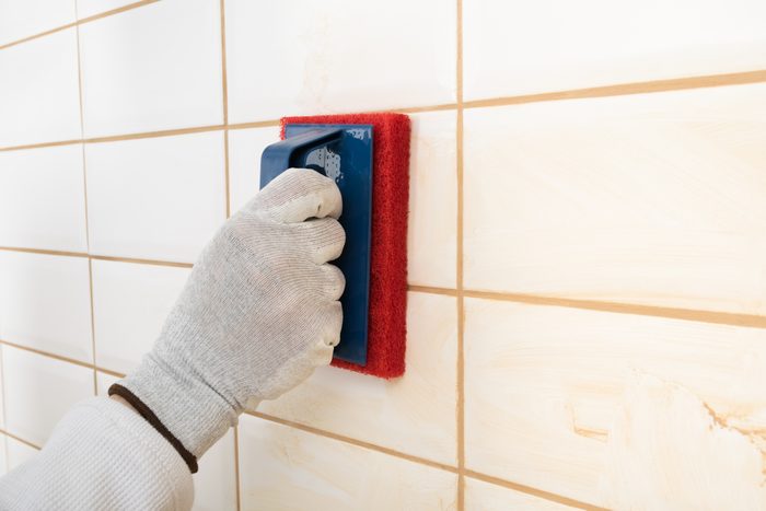 the hands of the master rubs the brown grout on white tiles with a special sponge, finishing work, close-up