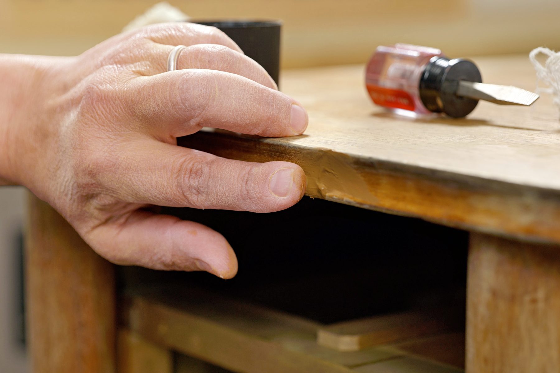 a close up shot of a person's hand lying on the table edge, A white cloth and a small screwdriver are also visible on the surface;