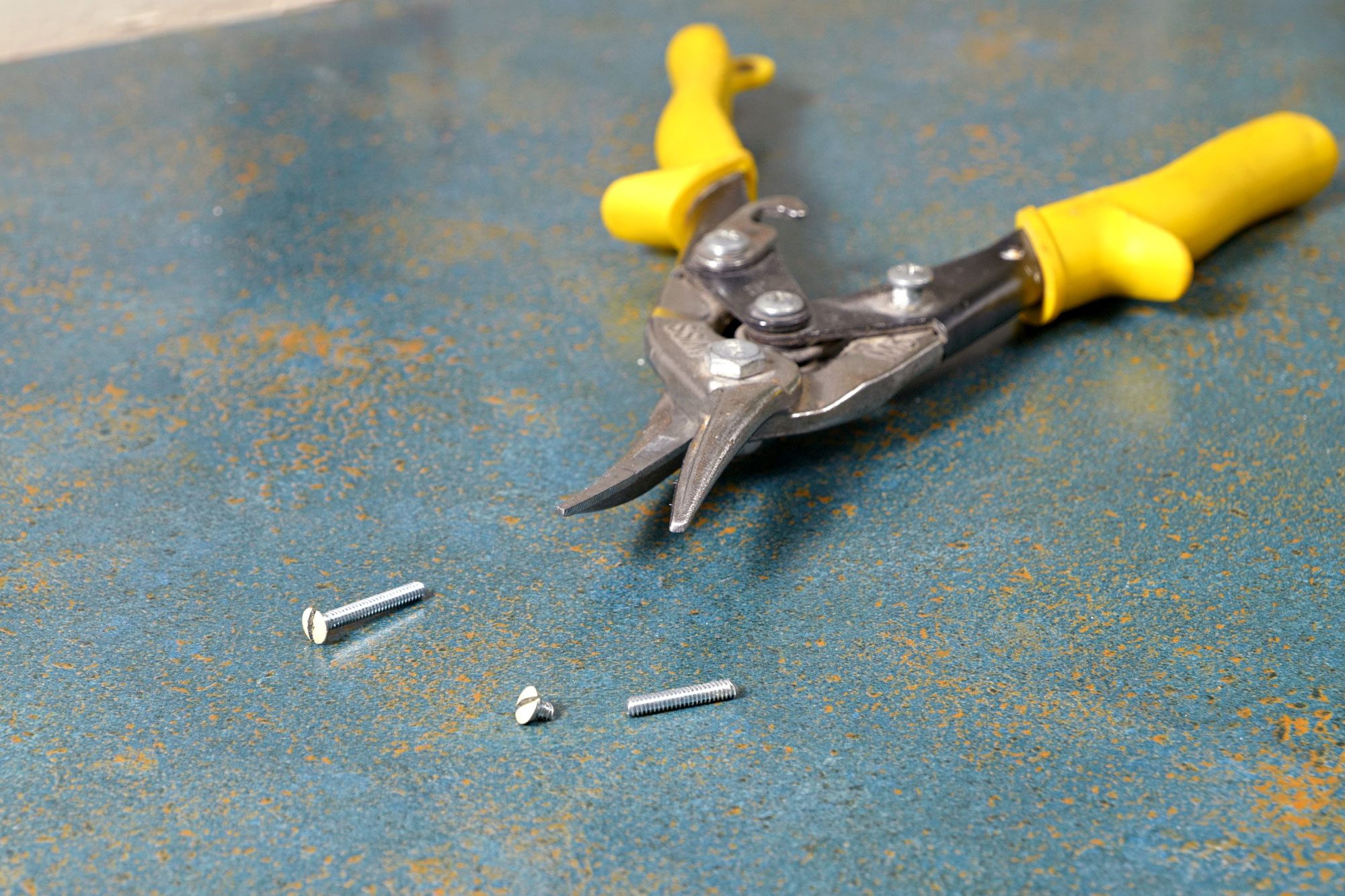 a pair of pliers with yellow handles lying on a blue speckled surface, There are also two small metal objects, which appear to be rivets, placed near the pliers;