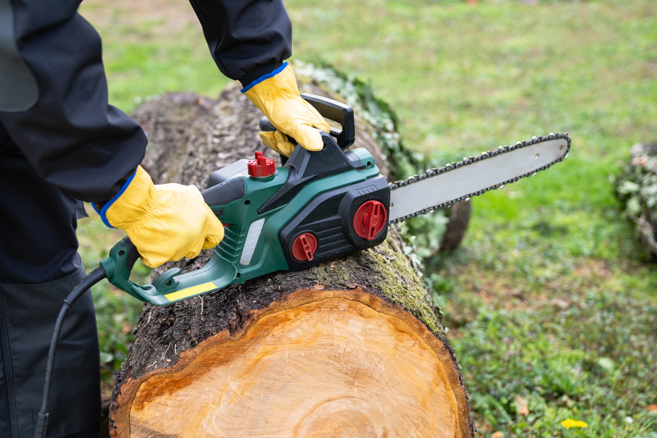 A man in uniform is cutting an old tree in the yard with an electric saw