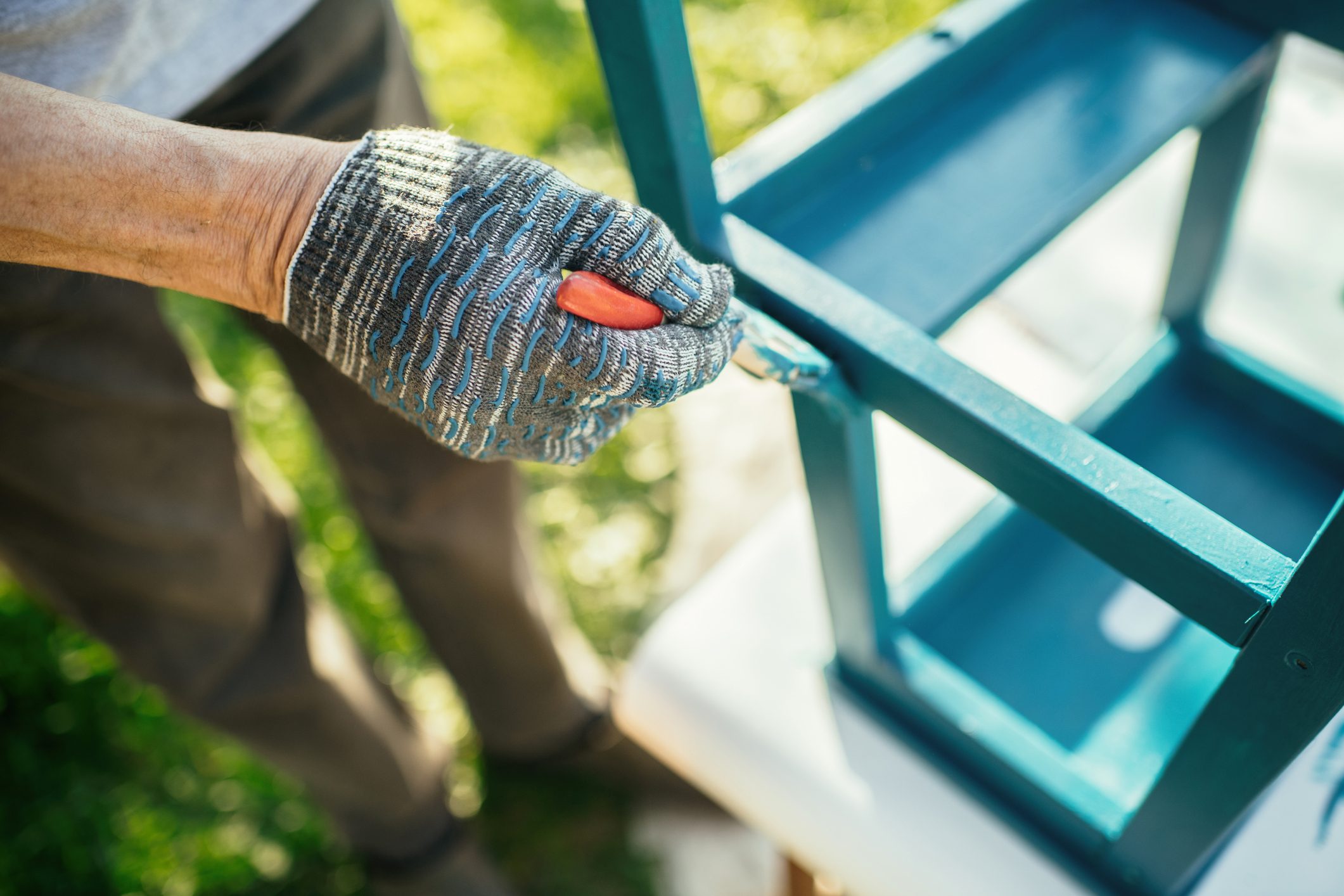 Senior man painting a chair outdoors at back yard in sunny evening. Old furniture renovation. Sustainability concept.