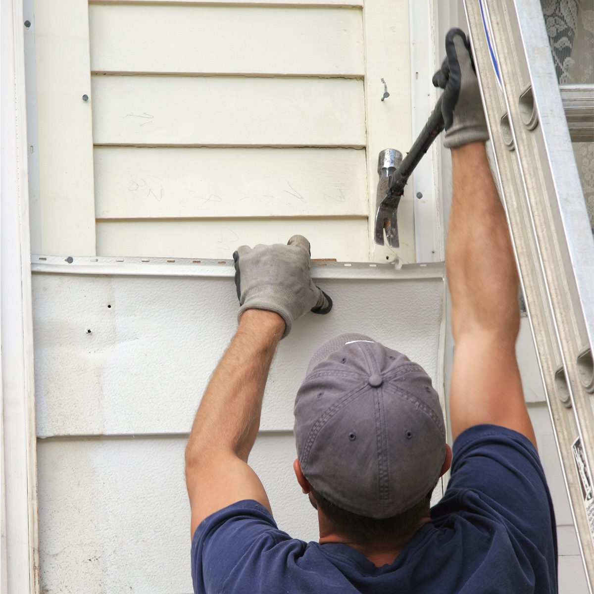 Silent Signs That Your House Has A Serious Problem Damaged Siding man in blue shirt, cap, and safety gloves