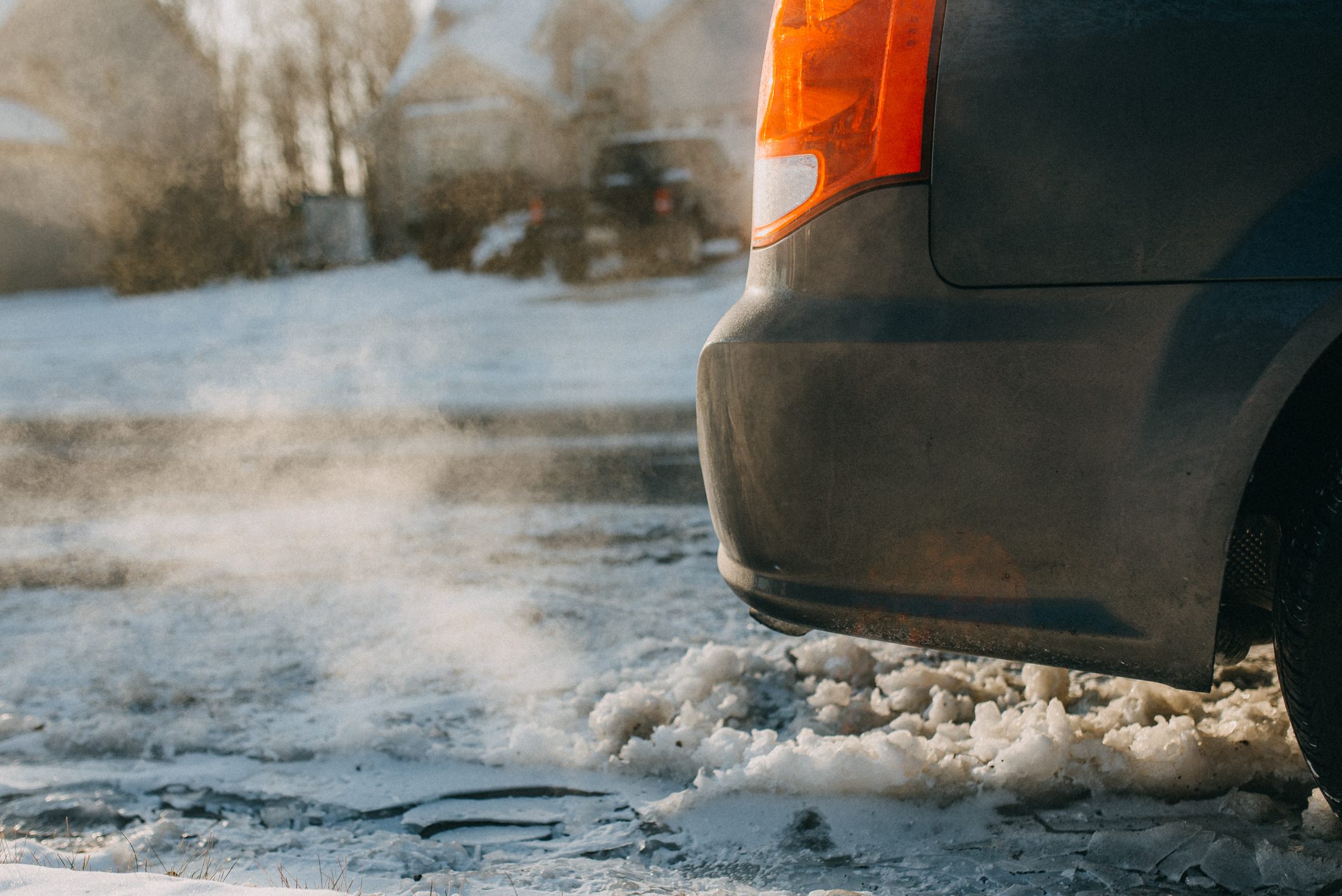 close up of exhaust and rear corner of a car idling on a snowy street in winter