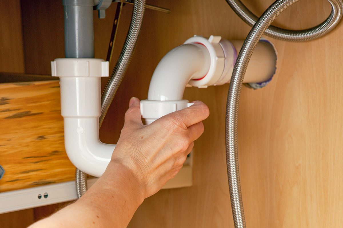 man reaching under sink to remove pipe