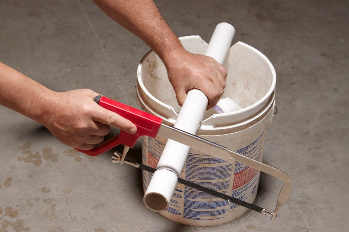 person sawing a pvc pipe over a bucket