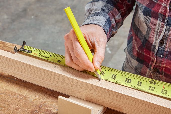 person using tape measure to make marking on wood