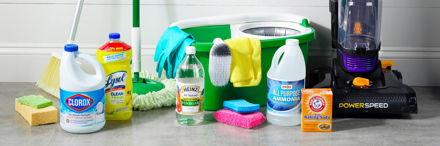 Cleaning Supplies arranged on a gray floor surface; clorox bleach, lysol, vinegar, ammonia, baking soda, sponges, broom, mop, bucket, vacuum