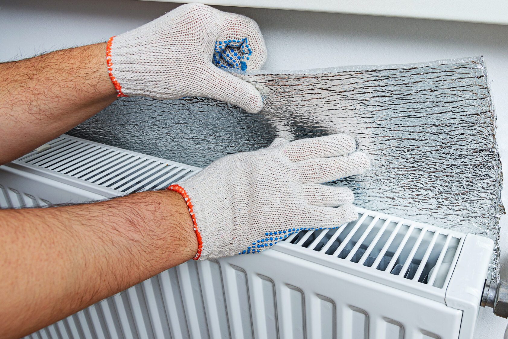 Installation of a polythene bubble film of aluminum foil thermal insulation on the wall behind the heating radiator