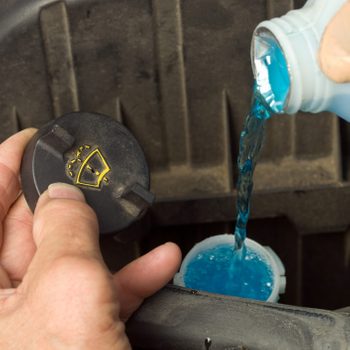 Male Hands Filling a Windshield Washer Reservoir with blue liquid