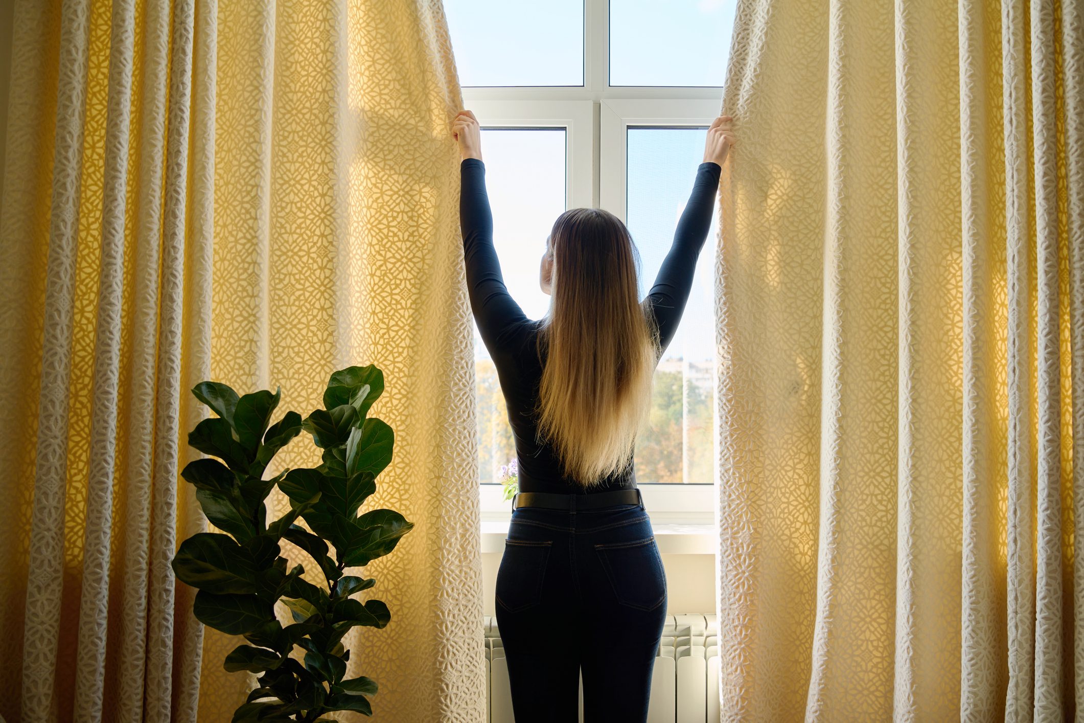 Young woman closing opening thick curtains on window