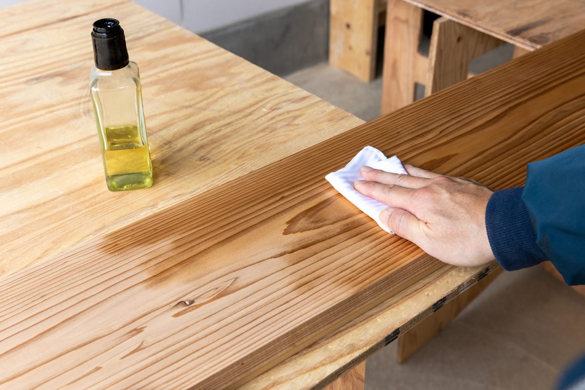 man wiping wood with a bottle of oil mixture nearby