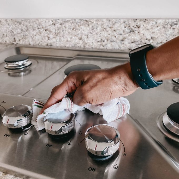 Hand wiping a stainless steel stove with a cloth