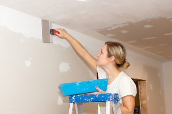 A young woman applying joint compound to a ceiling joint