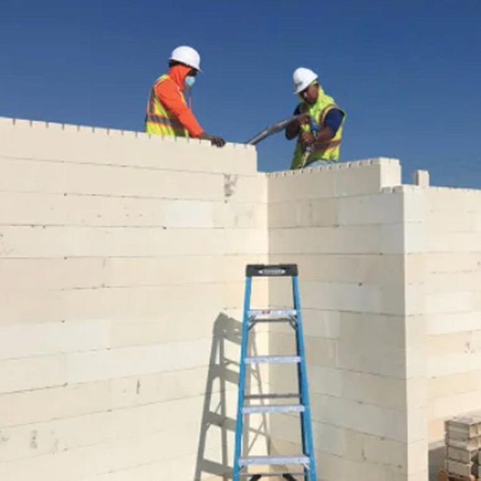 Two construction workers stand on top of a wall made of Renco bricks, with a blue ladder in front